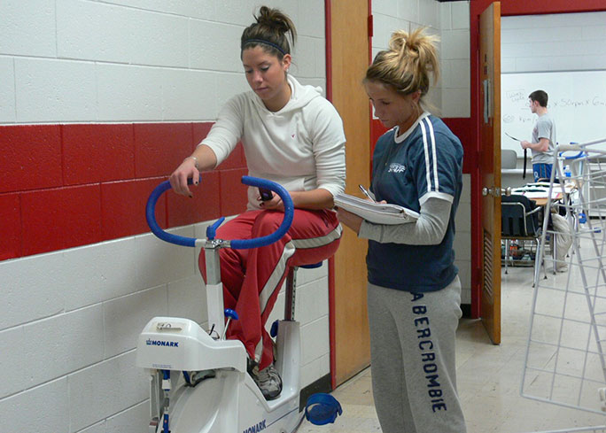 One student studies another working on an elliptical machine