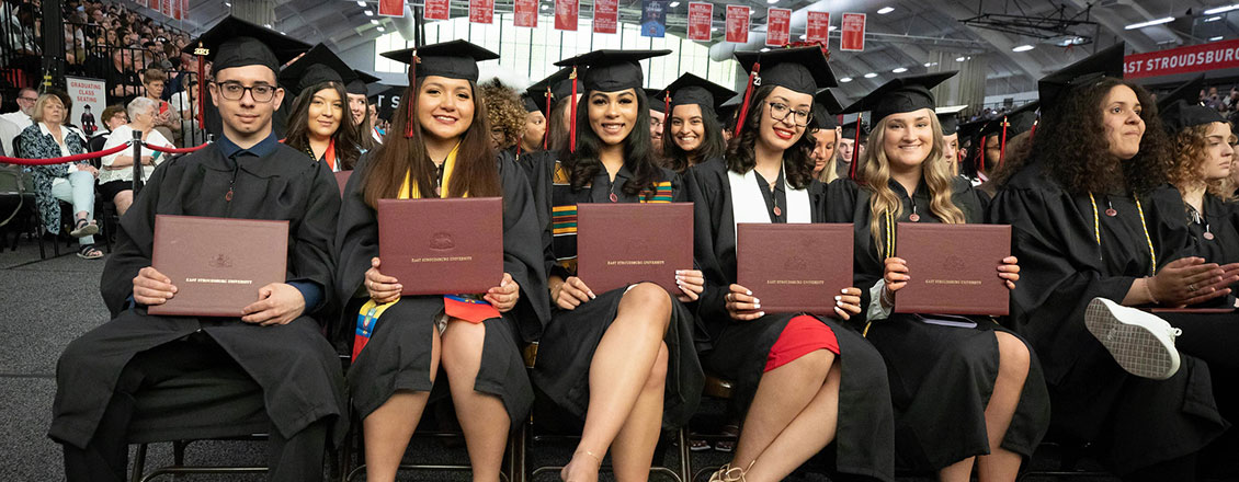 5 students holding diplomas during commencement