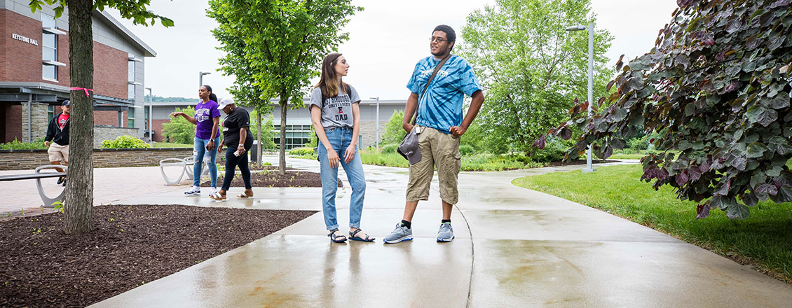 Two students stand together outside, one each wearing NCC and ESU t-shirts