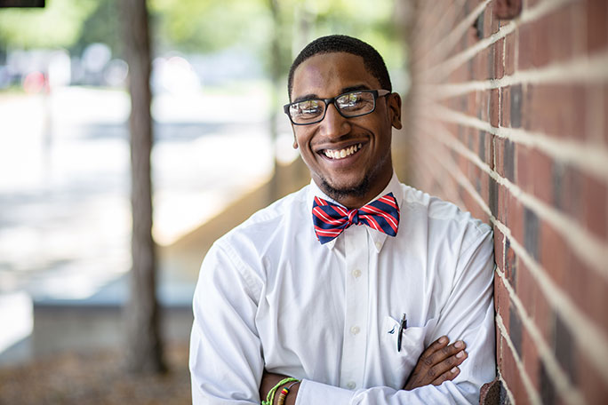 student leaning against wall wearing bowtie