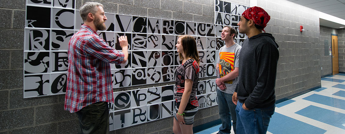 Students and a faculty member looking at an artistic periodic table mounted on a large wall