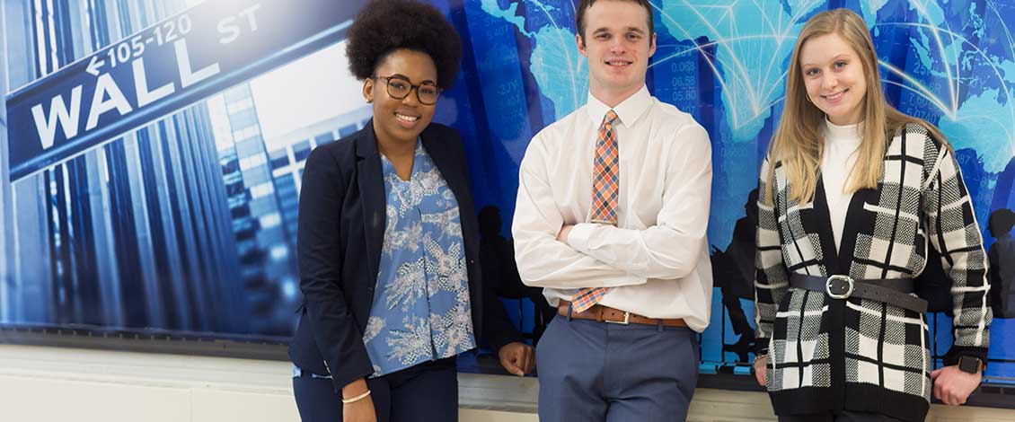 three students standing at board with wall street behind them