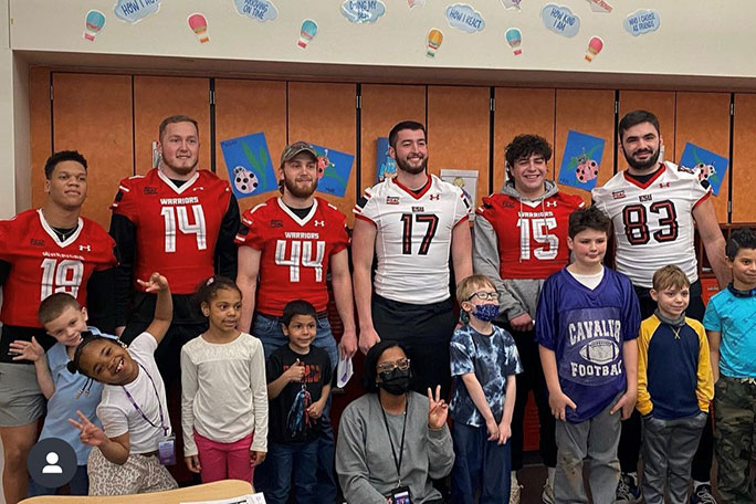 warrior football players standing with grade school students