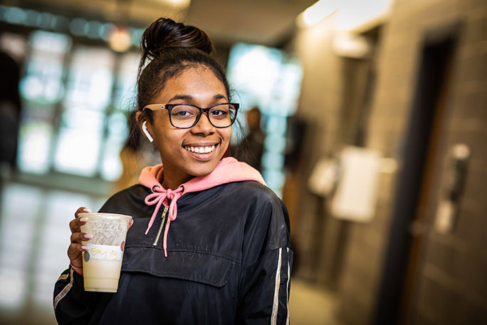 A student smiling and holidng a coffee cup