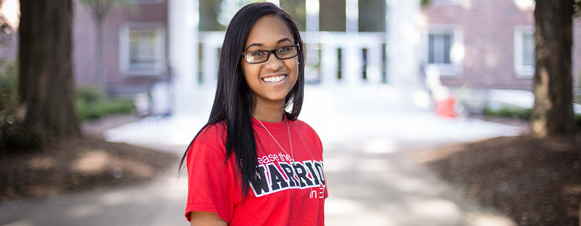female student standing in front of stroud hall with esu shirt on