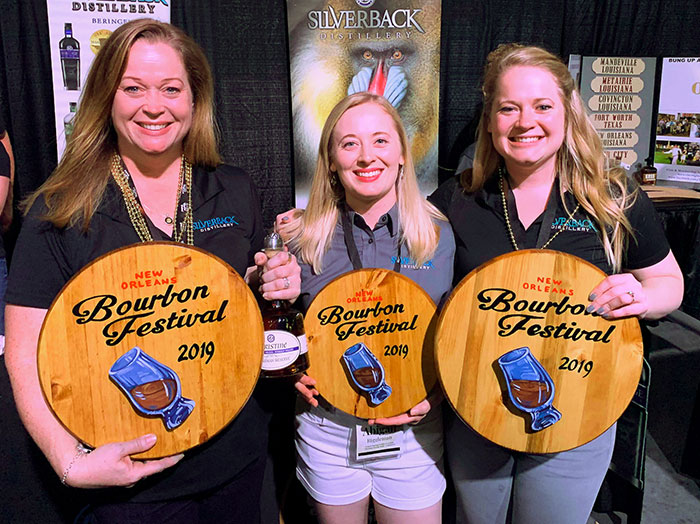 Christine, Lauren and Abby Riggleman holding signs and a bottle of bourbon