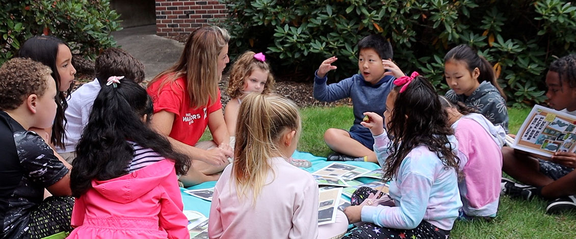 Kids sitting in a circle outside on a blanket discussing a nature story