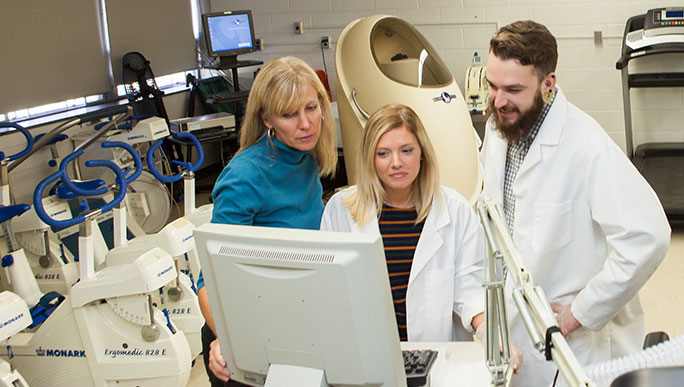 Students and a faculty member working on a PC surrounded by exercise science equipment