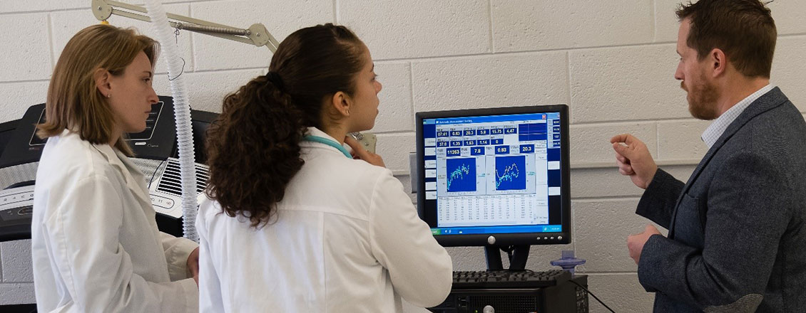 2 female students in lab coats discussing results with instructor