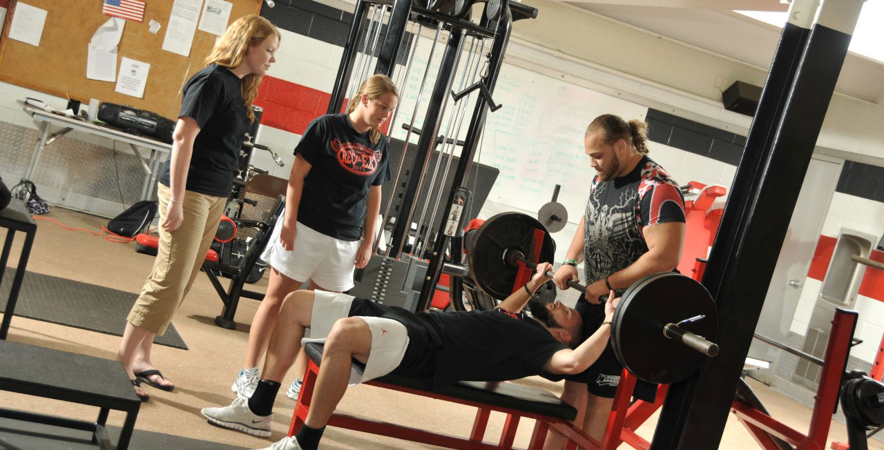 Students observing someone exercising in a weight room