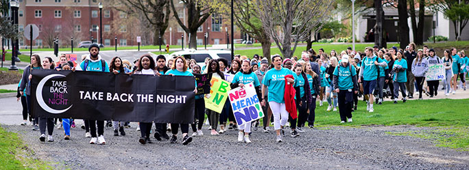 Dozens of students marching together, some carrying a large banner reading Take Back the Night