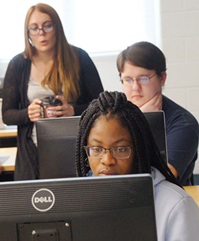 Three students working at computers, two collaborating