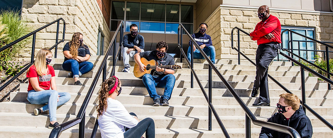 Interim President Kenneth Long standing a steps of Sycamore Suite with students and a guitar player