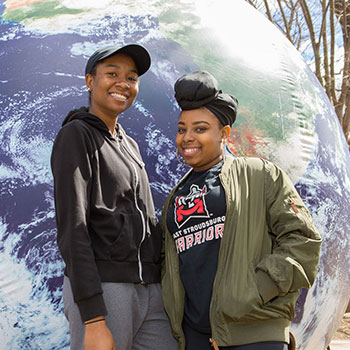 two female students standing in front of a giant global.