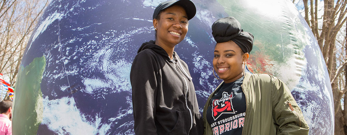 two female students standing in front of giant globe