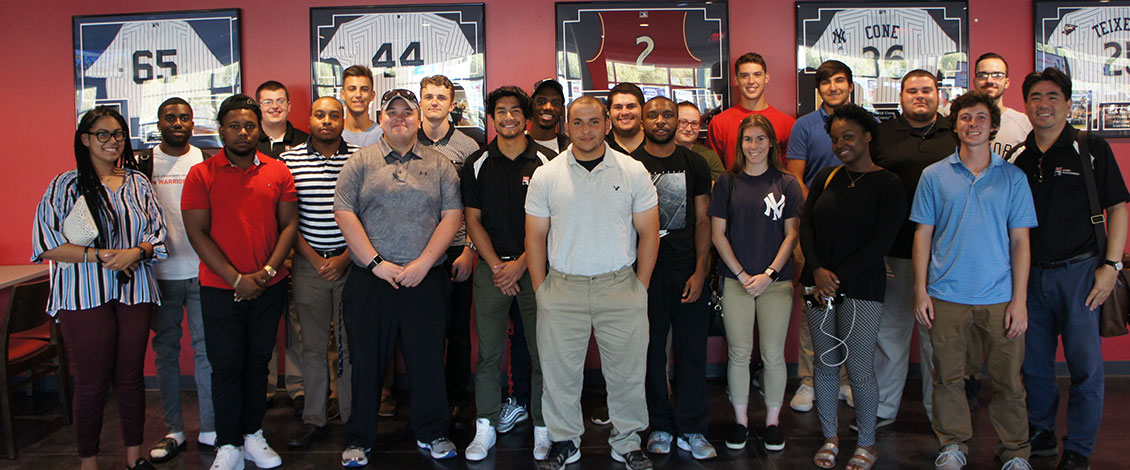 Sport Management students on a tour, standing in front of framed baseball jerseys