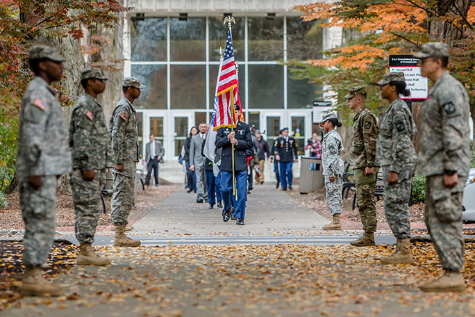 People in military uniform march for Veterans Day holding the U.S. flag